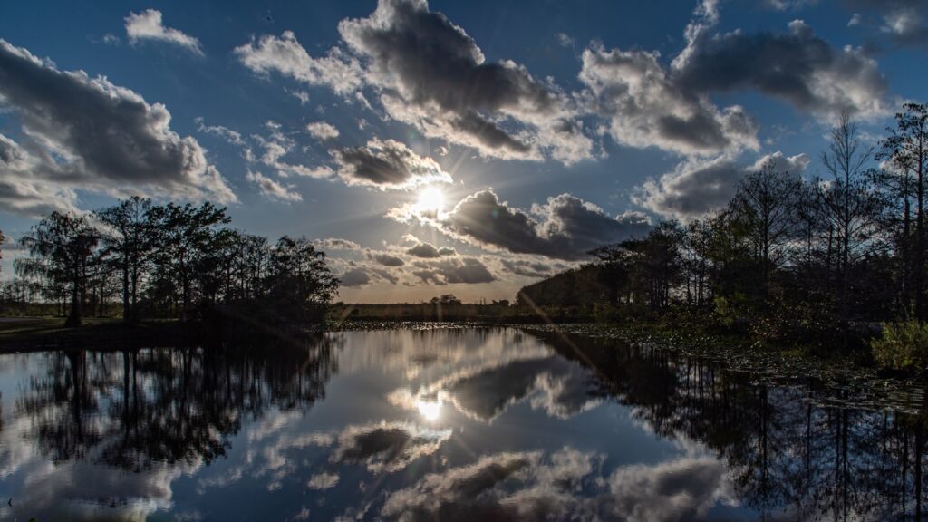 the sun shining through the clouds over a lake surrounded by trees