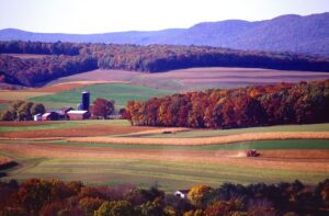 Scenic landscape of rolling hills and farmland with a farm house and barn in the foreground