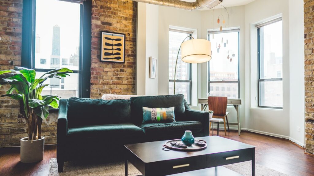 green sofa against a brick brownstone wall with a white bay window