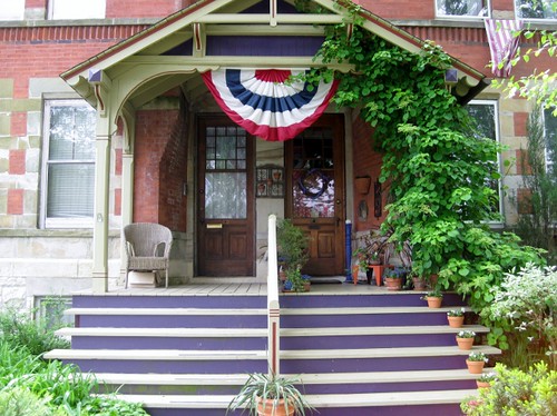 Front porch of a red brick building with stairs and a decorative awning with trailing vines up the side