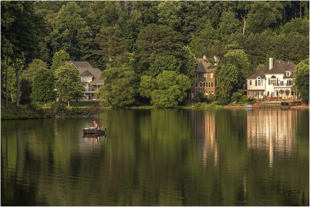 small boat on a lake with homes on the shore and green trees