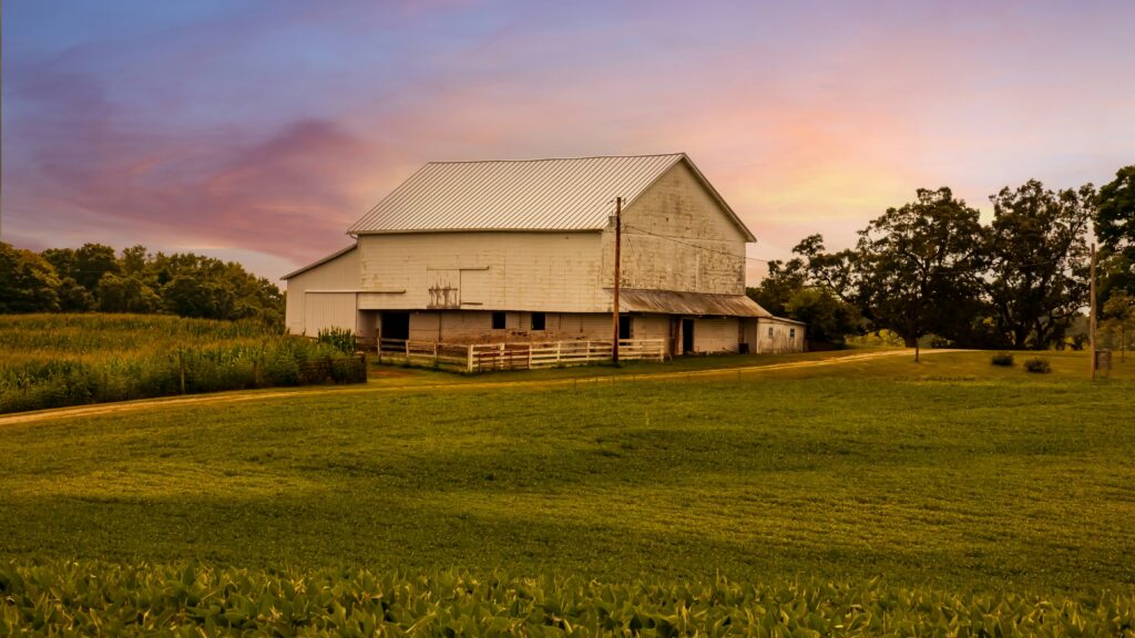 A white barn silhouetted against a sunset sky and surrounded by trees