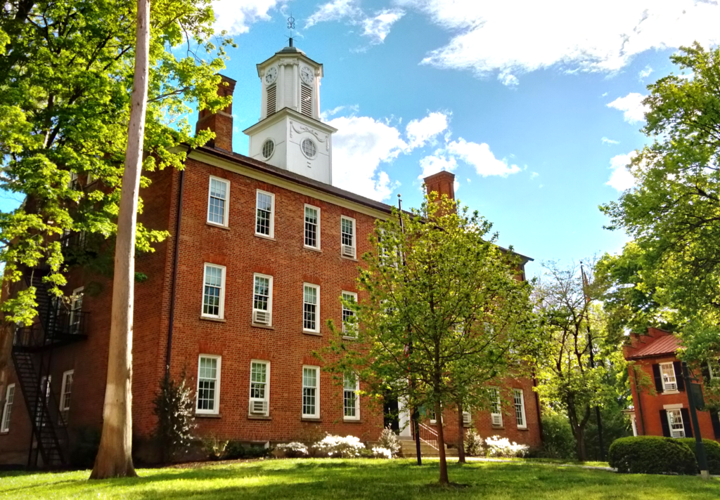 A red brick building with a white spire on top surrounded by green trees