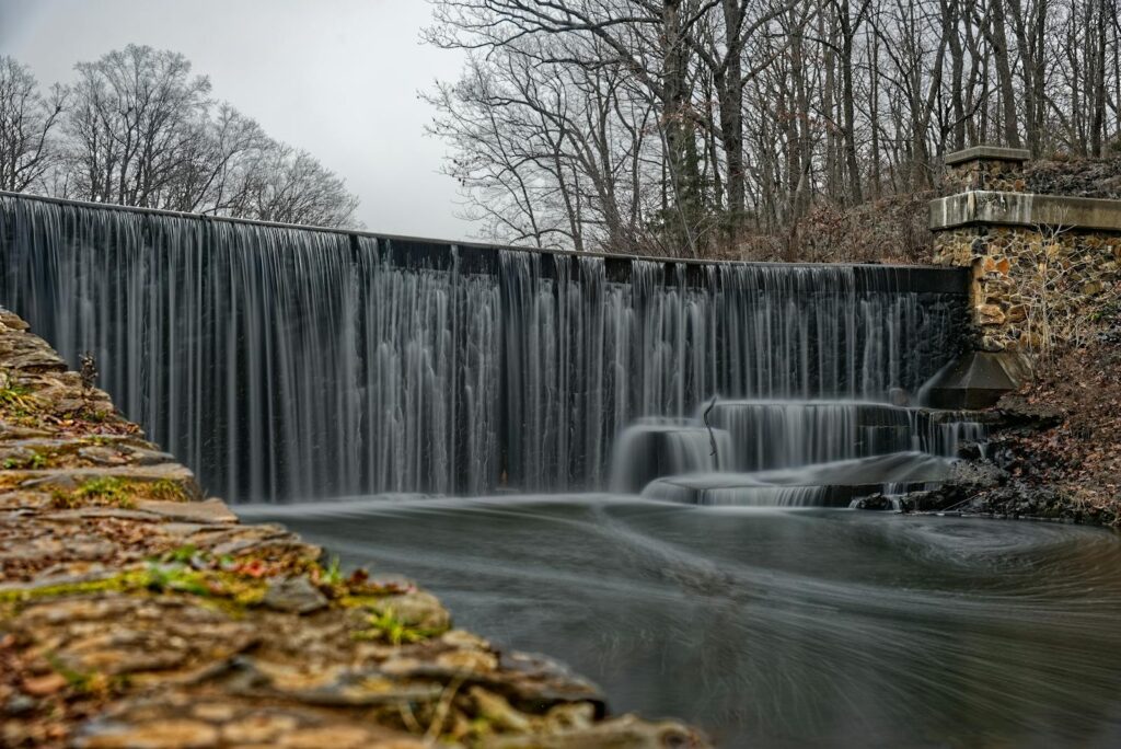 Serene waterfall flowing over stone dam in New Jersey park surrounded by bare winter trees.