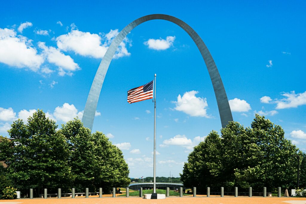 us flag on pole near trees during daytime in the center of a silver arch landmark