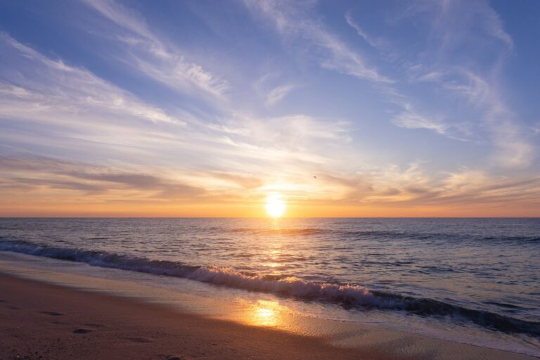 the sun is setting over the ocean on the beach